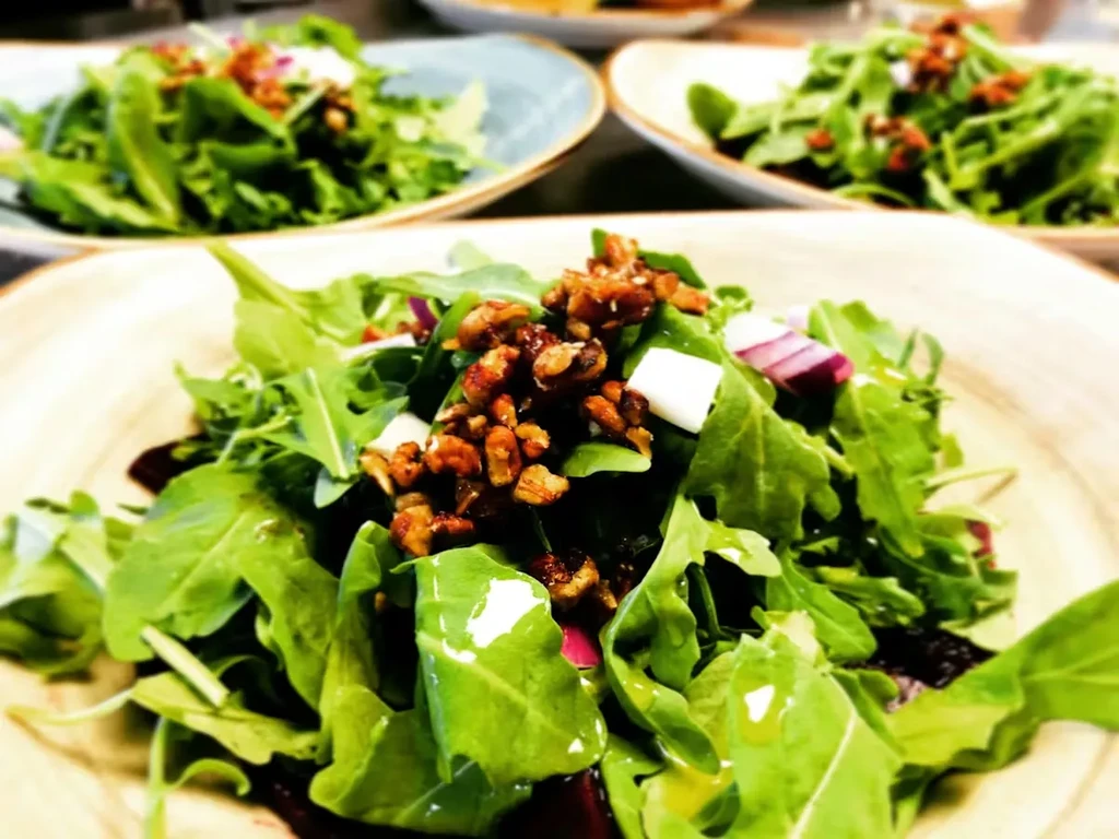 Three plates of green salad with nuts, white cheese, onion, and dressing.