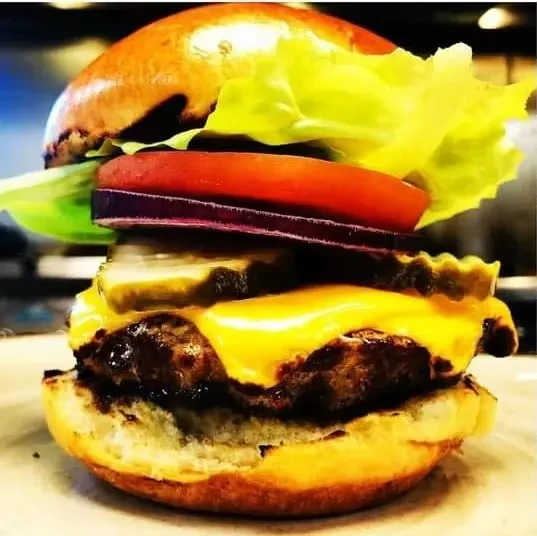A layered cheeseburger with melted cheese, lettuce, tomato, onion, and pickles.