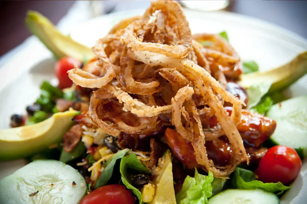 Close-up of a salad topped with crispy fried onion rings and vegetables.