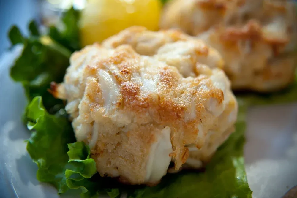Two golden-brown crab cakes with visible meat, on lettuce and lemon.