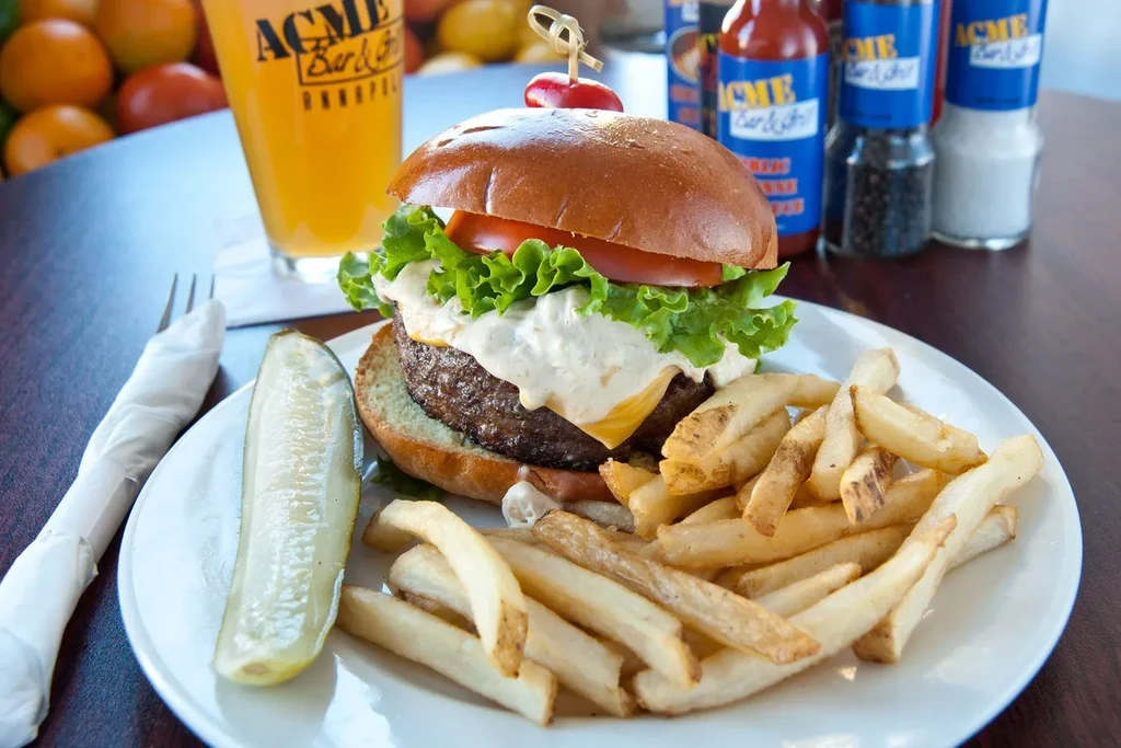 Burger with melted cheese, white sauce, lettuce, tomato, fries, and pickle.