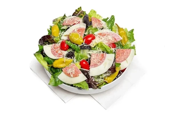 Fresh salad in white bowl with lettuce, tomatoes, cheese, salami.