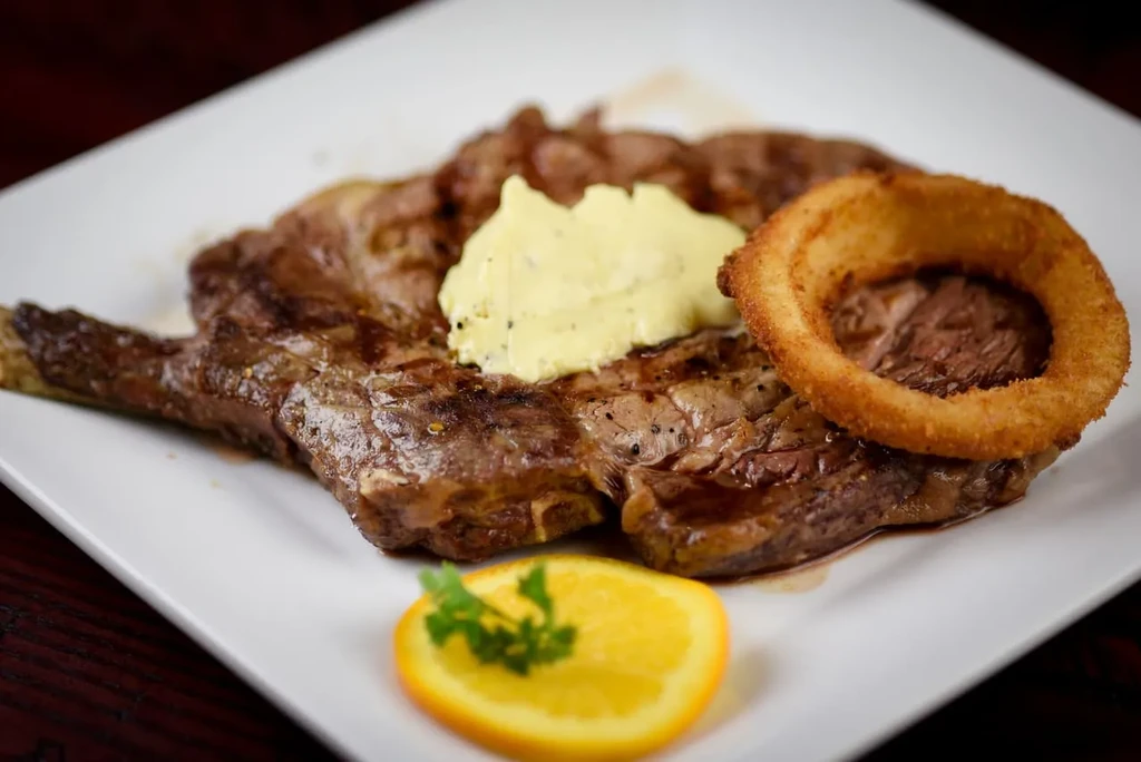 Grilled steak with herb butter, crispy onion ring, and orange garnish.