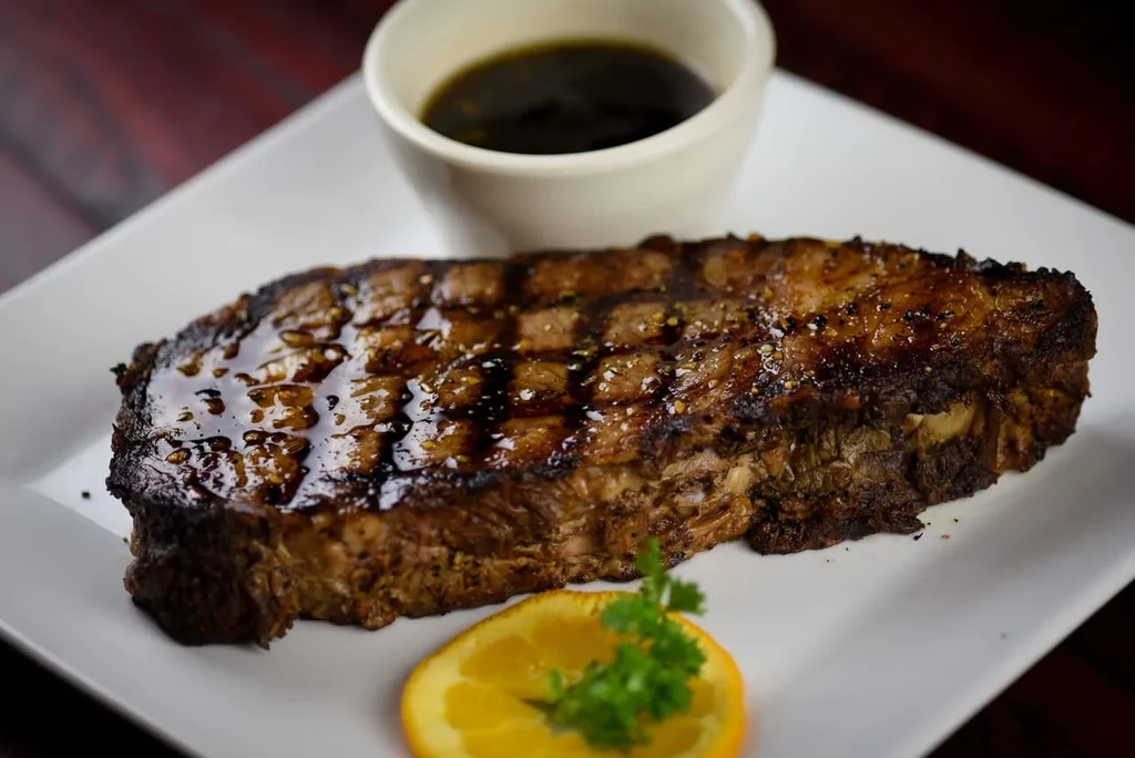 Grilled meat with char marks, dipping sauce, orange slice, and parsley.