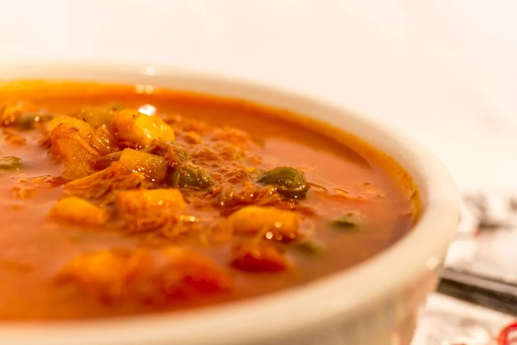 Bowl of thick reddish-orange stew with vegetables and shredded ingredients.