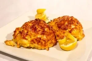 Two golden-brown crab cakes with lemon wedges on a white plate.
