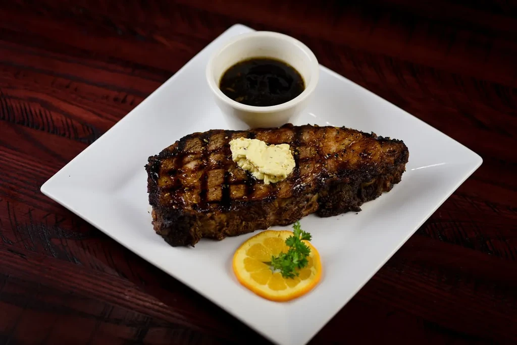 Grilled steak, herb butter, dark sauce, and orange garnish on wood.
