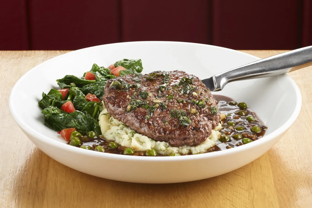 Meat patty with herb sauce, mashed potatoes, spinach, and peas.
