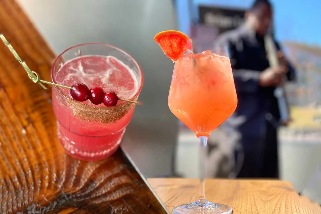 Pink and orange cocktails with garnishes; blurred musician playing.