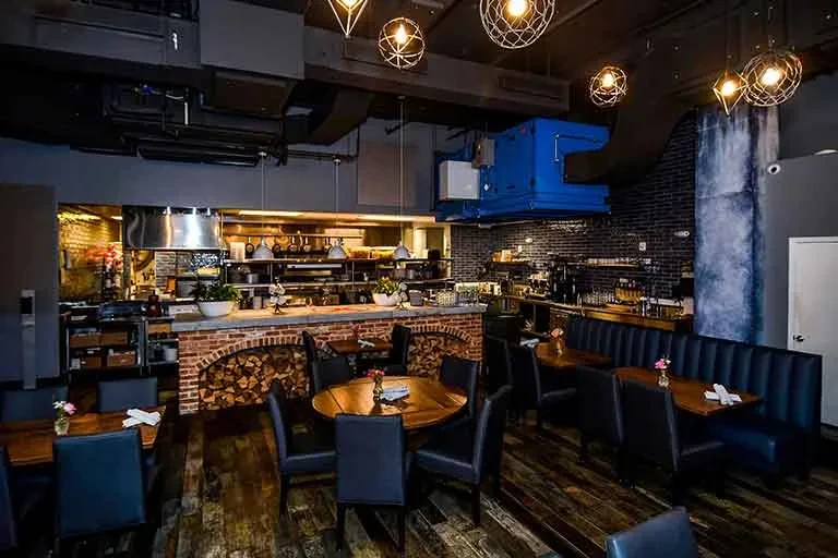 Industrial-chic restaurant with open kitchen, brick details, and warm lighting.