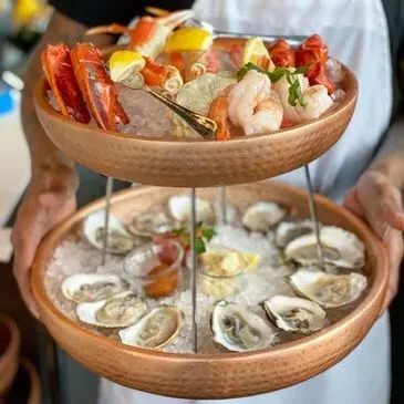 Two-tiered seafood tower with crab legs, shrimp, and oysters on ice.