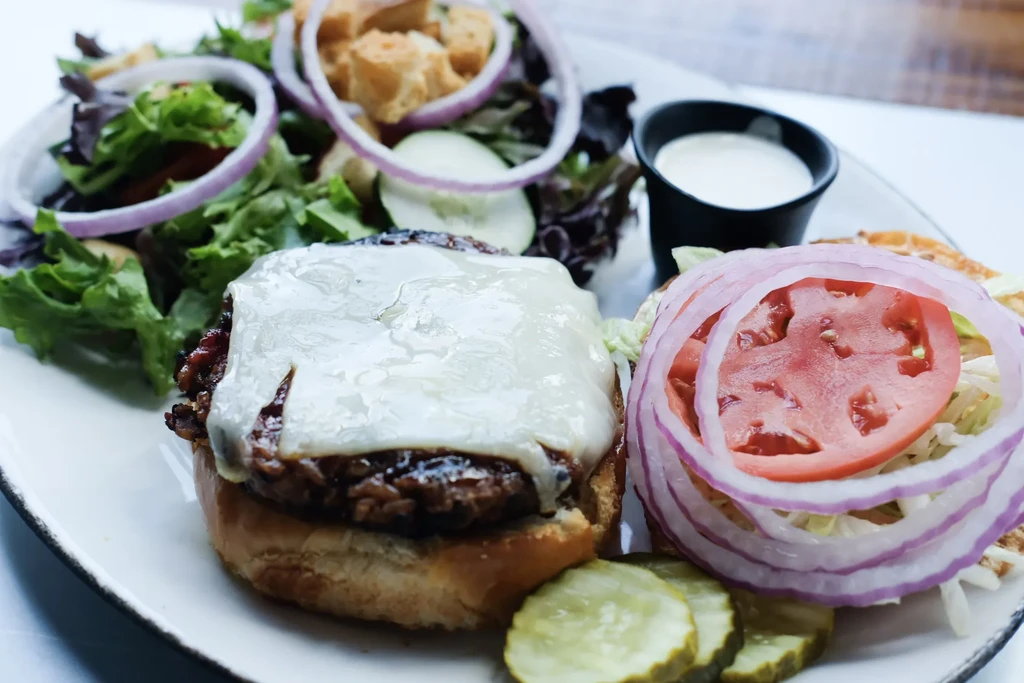 Open-faced cheeseburger, separate bun, pickles, and a green side salad.