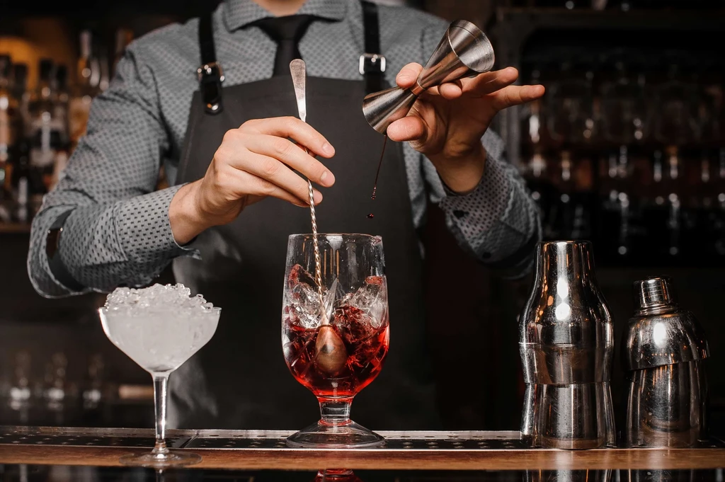 Close-up: Bartender pouring and stirring a red cocktail at a bar.