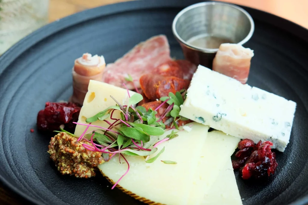 Charcuterie board with cheeses, meats, mustard, preserves, and microgreens.