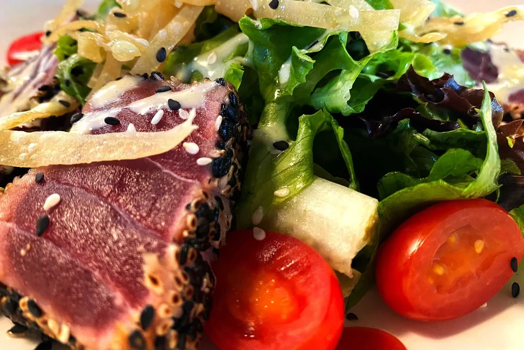 Close-up: Seared sesame tuna steak with sauce, garnish, and fresh salad.