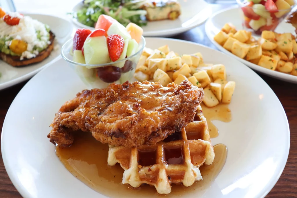 Fried chicken and waffle with syrup, fruit salad, and potatoes.