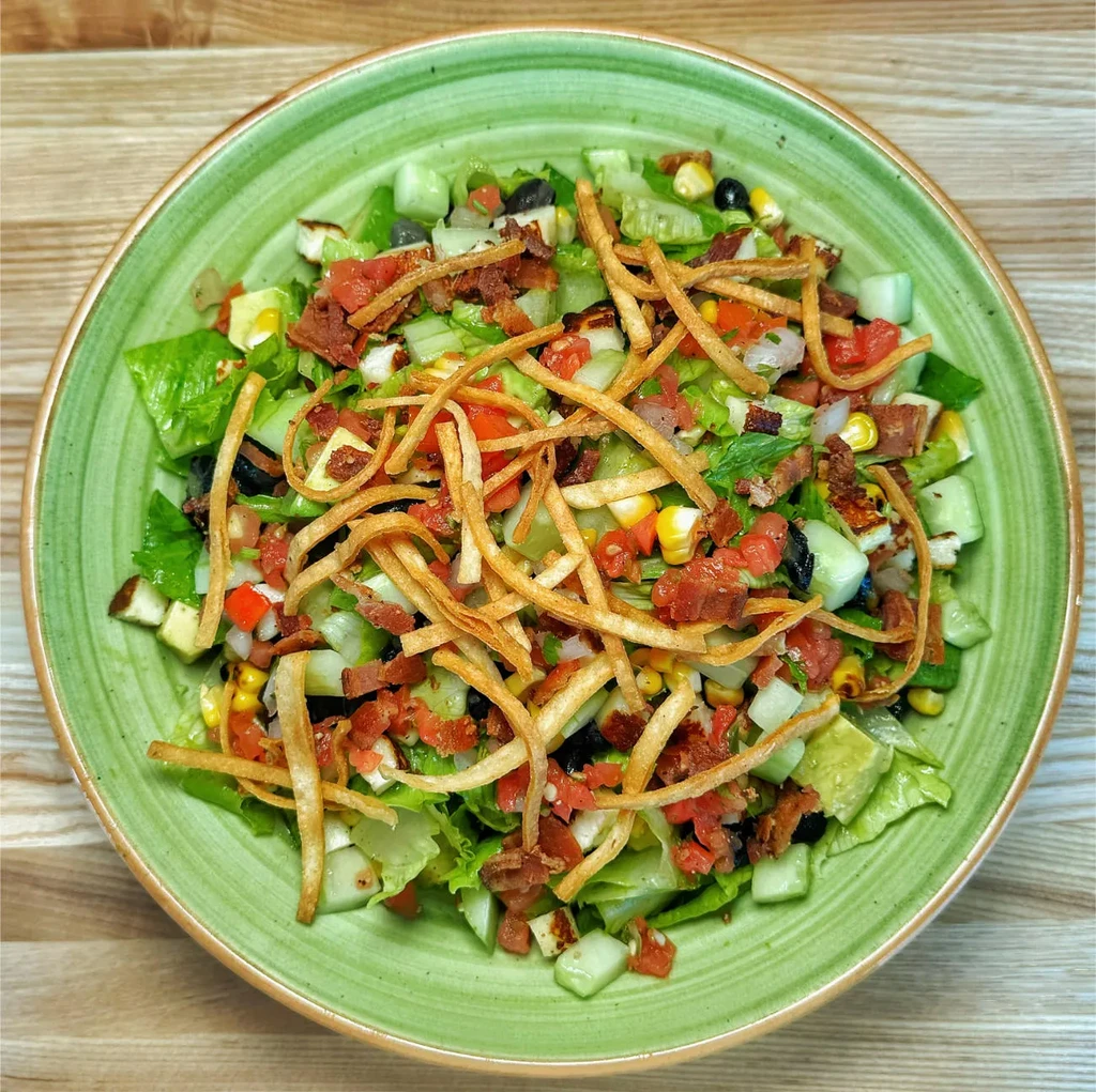 Vibrant salad with chicken, vegetables, and crispy toppings in a green bowl.