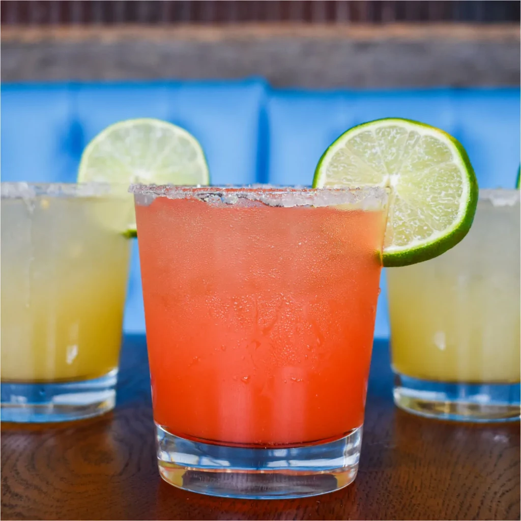 Three vibrant margaritas: one reddish-orange, two yellowish-green, on wood.