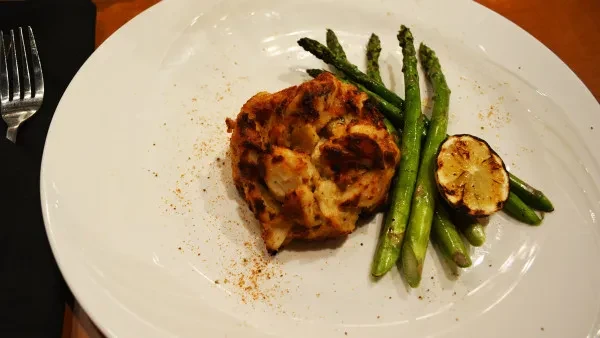 Golden crab cake, green asparagus, and grilled lemon on white plate.