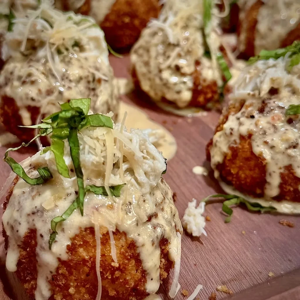 Crispy fried spheres topped with creamy sauce, shredded cheese, and green herbs.