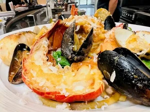 Vibrant seafood pasta with prominent lobster tail, mussels, and cheese.