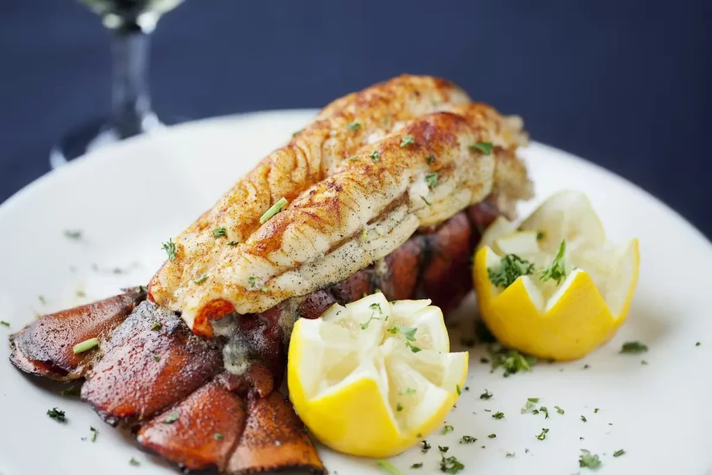 Seasoned golden-brown lobster tail plated with lemon halves and fresh herbs.