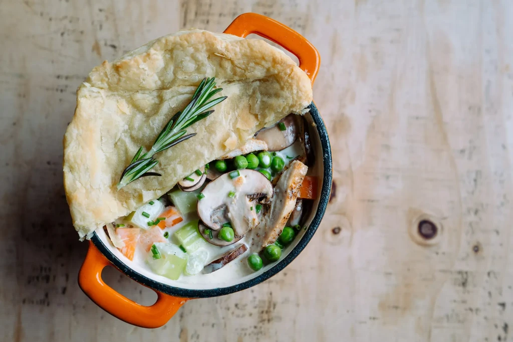 Chicken and vegetable pot pie with flaky crust and rosemary garnish.
