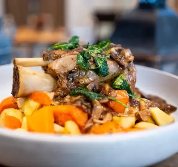 Meat shank with prominent bone, dark sauce, mushrooms, carrots, and herbs.