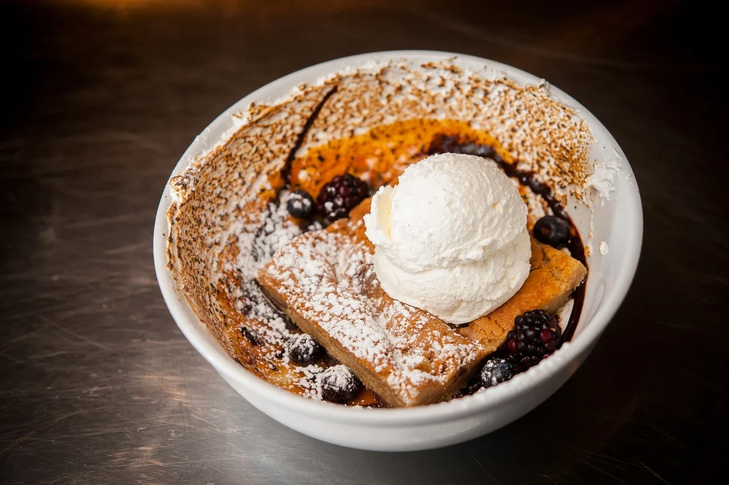 Puffy pancake, powdered sugar, ice cream, berries, and syrups in a bowl.