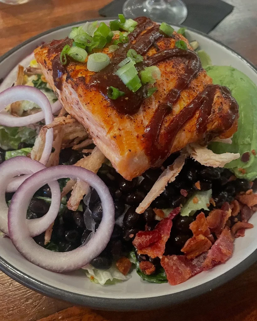 Seared salmon with salad, avocado, and black beans in a bowl.
