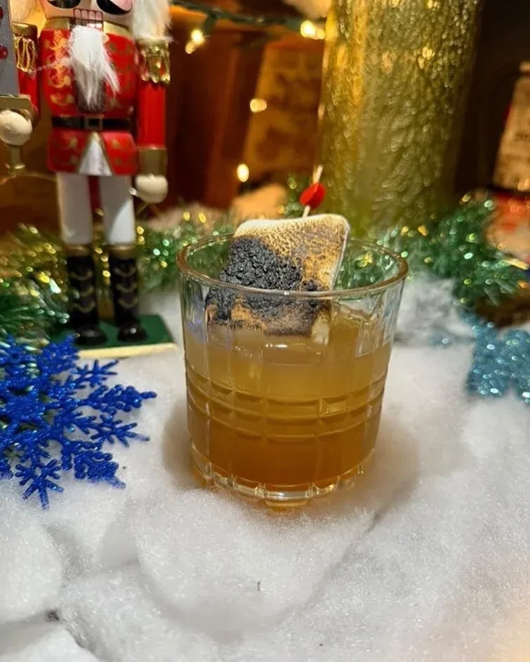 Amber cocktail with charred marshmallow on a snowy holiday display.