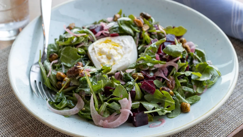 Salad with burrata, beets, green leaves, and candied nuts in a bowl.