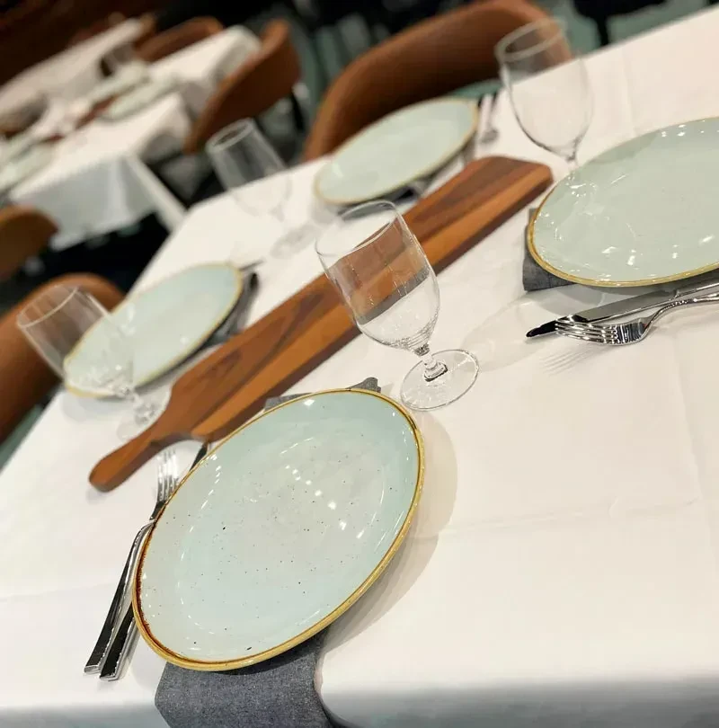 Restaurant table set with plates, glasses, cutlery, and a wooden board.