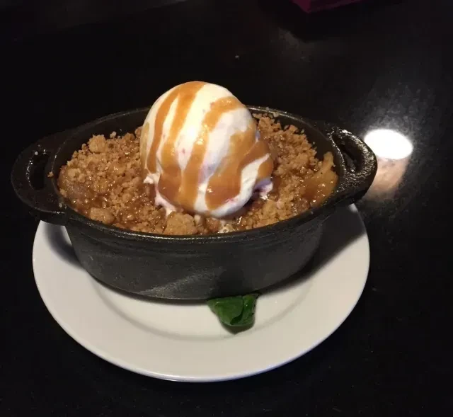 Apple crumble in cast-iron pot with vanilla ice cream, caramel drizzle.
