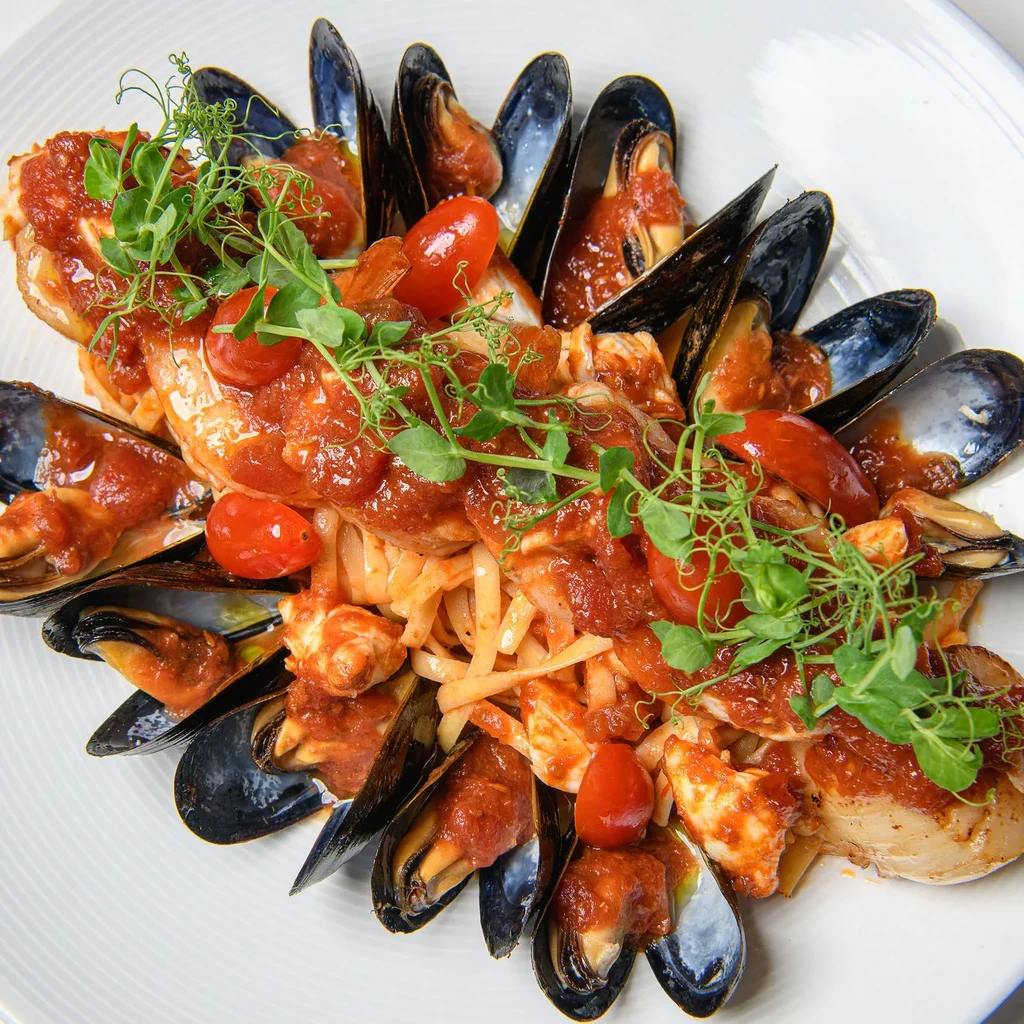 Seafood pasta with mussels, white seafood, tomatoes, and microgreens.