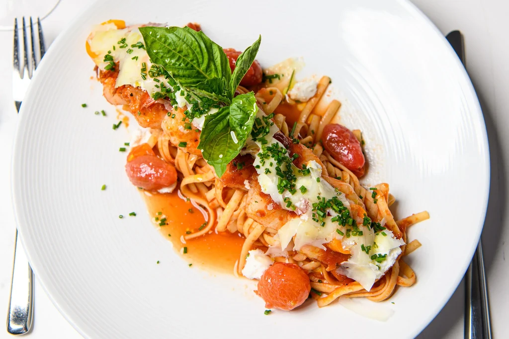 Plated pasta with shrimp, tomato sauce, cheese, cherry tomatoes, and fresh herbs.