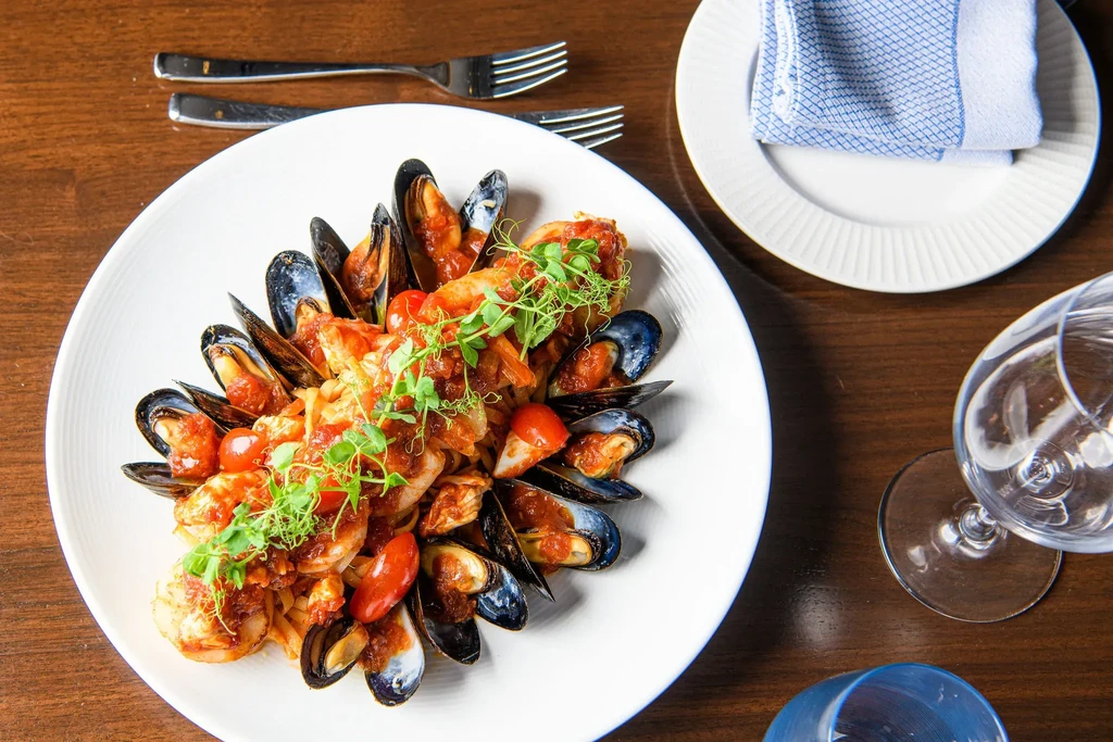 Overhead view of seafood pasta with shrimp, mussels, tomatoes, and microgreens.