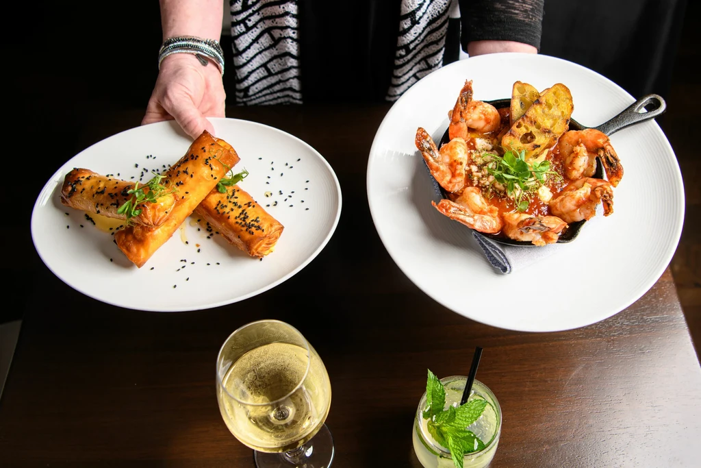 Overhead view of hands holding plates of shrimp and appetizers, with drinks.