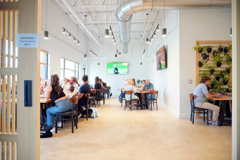 Bustling modern restaurant interior with diners, exposed ductwork, and living wall.