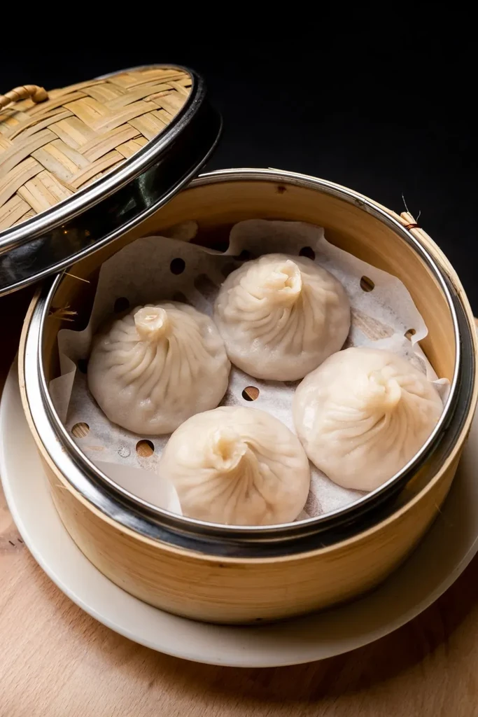 Four steamed soup dumplings in a partially open bamboo steamer.