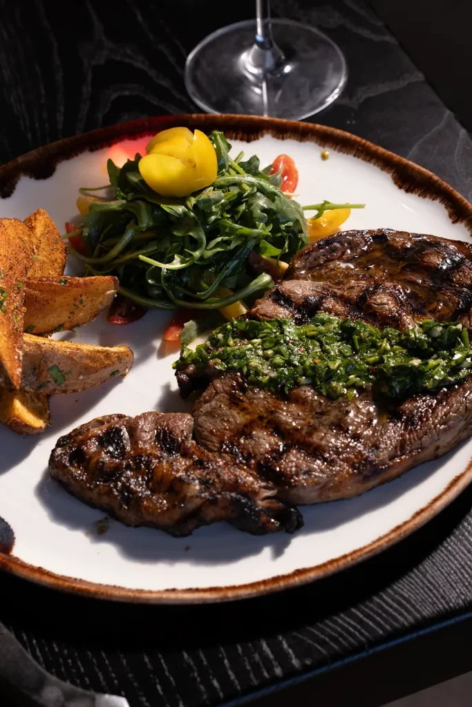 Grilled steak with chimichurri, potato wedges, and arugula salad.