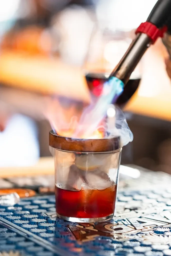 Close-up of a cocktail flaming with a torch, smoke rising.
