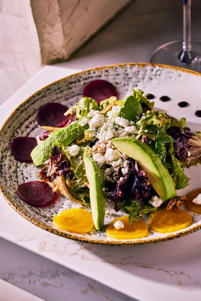 Fresh plated salad with greens, avocado, white cheese, nuts, and beets.