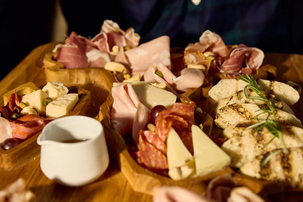 Rustic wooden charcuterie board piled with meats, cheeses, bread, grapes, nuts.