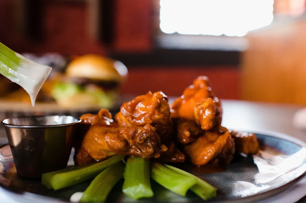 Orange-red chicken wings, celery sticks, one dipping into white sauce.