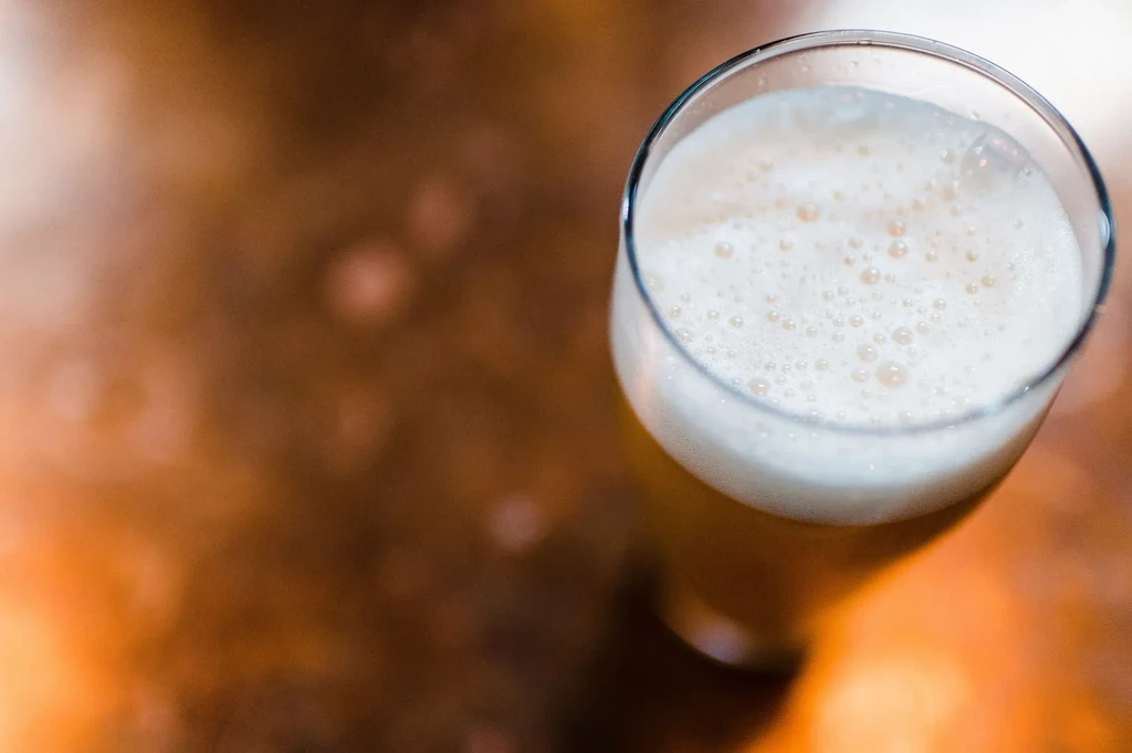 Close-up of a glass of amber beer with thick white foam.