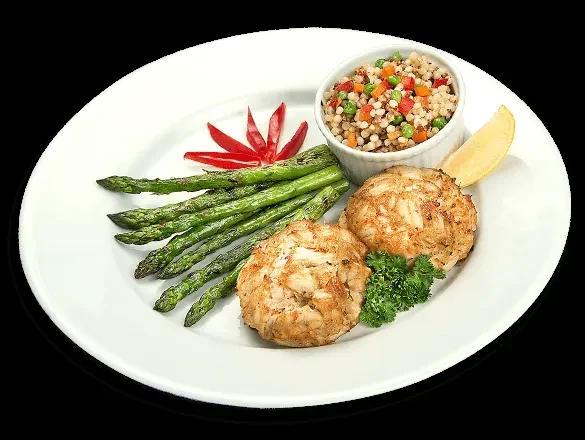 Two crab cakes, asparagus, grain salad, lemon, and parsley on a plate.