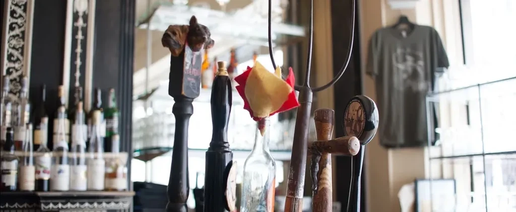 Detailed beer taps and many liquor bottles behind a bright bar.