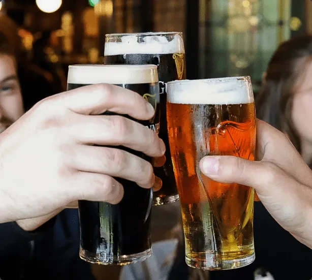 Three hands toast two dark beers and one amber beer.