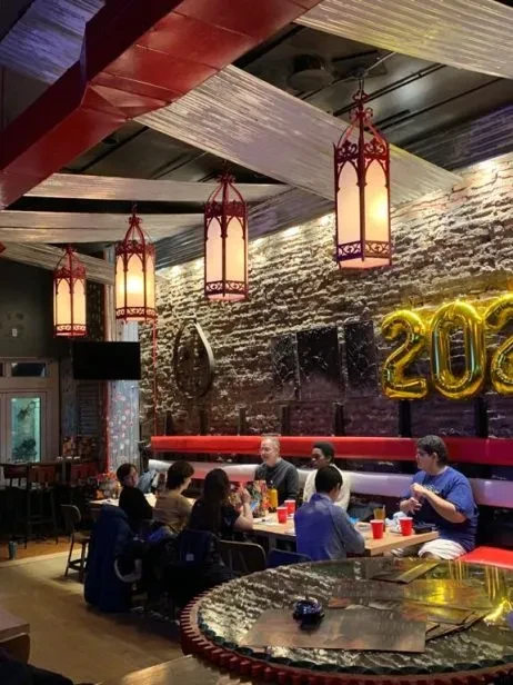 Group of diners in industrial-chic restaurant with '2023' balloons.